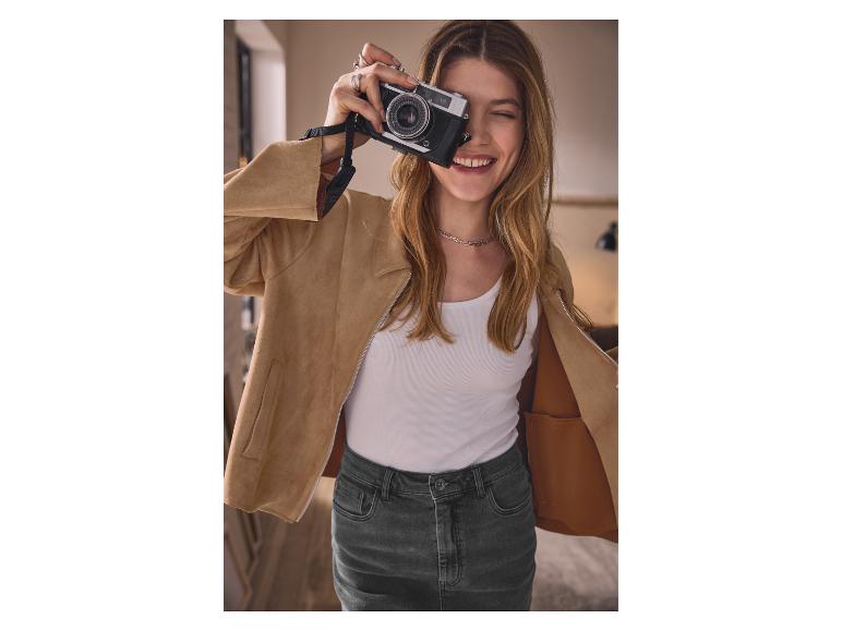 Femme en veste beige et jupe en jean, prenant une photo avec un vieil appareil photo.