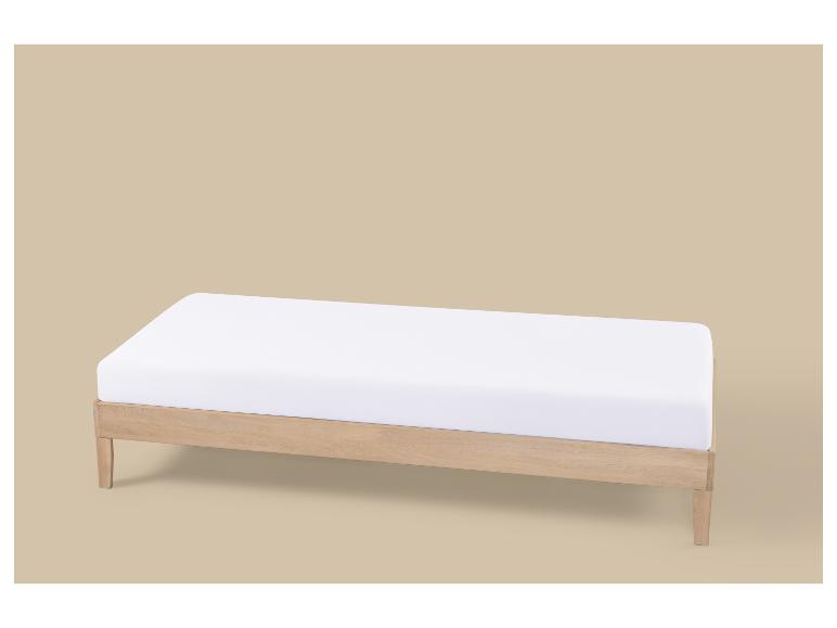 Lit simple en bois clair avec matelas blanc sur fond beige.