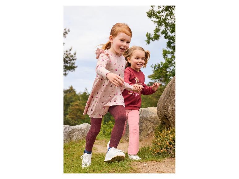 Deux filles en tenues d'automne courent main dans la main en extérieur.