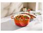 Cocotte orange remplie de légumes sur un comptoir avec des épices et un torchon.