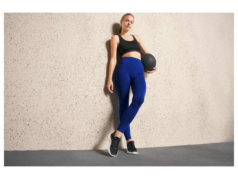 Une femme en leggings bleus et en baskets noirs tient un ballon de médecine.