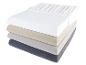 Une pile de quatre draps-housses : blanc, beige, gris et gris foncé.