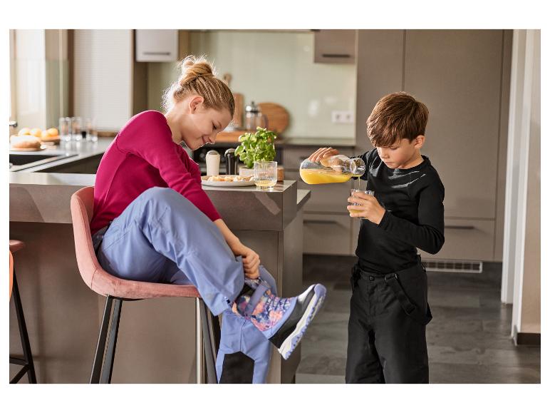 Femme et enfant dans la cuisine, l'enfant verse du jus, la femme met ses bottes.