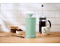 Moulin à café vert menthe, cafetière à piston et café moulu sur un comptoir en bois.