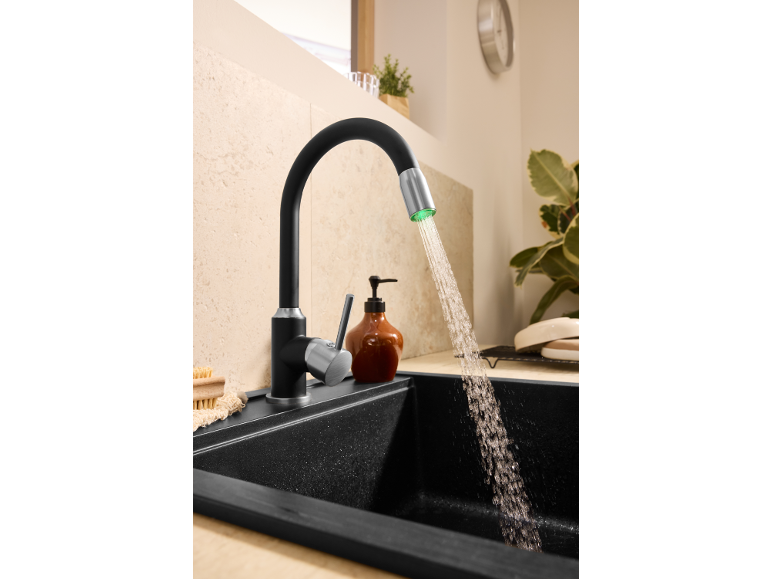 Robinet de cuisine noir avec lumière LED verte et eau courante dans un évier noir.