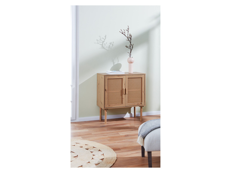 Une commode en bois avec des portes en rotin, un tapis rond en jute et un pouf gris.
