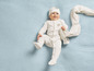 Un bébé dans une combinaison blanche et un bonnet avec un motif de nuages sur une couverture bleue.