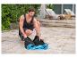 Homme pliant un tapis d'exercice bleu sur une terrasse pavée.