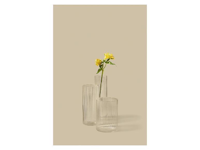 Trois vases en verre côtelé, l'un avec des fleurs jaunes, sur fond beige.