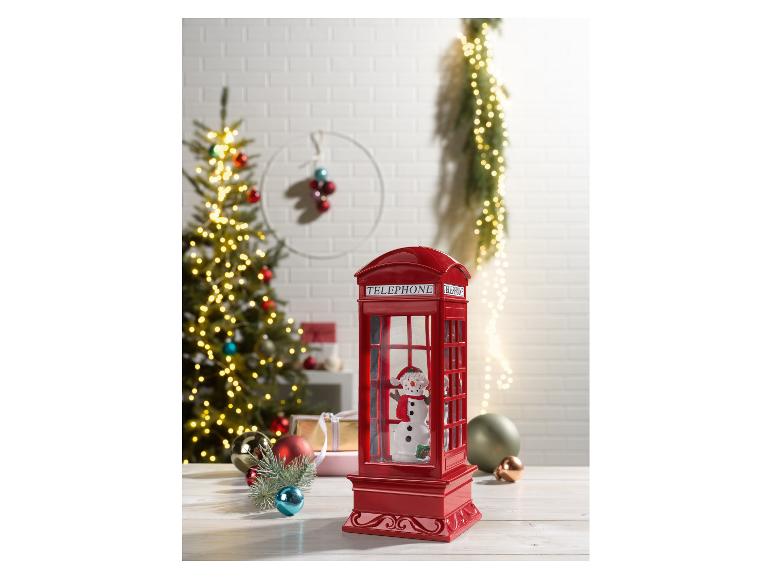 Cabine téléphonique rouge de Noël avec un bonhomme de neige, entourée de décorations festives.