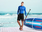 Un homme avec une planche de paddle surf Mistral et des vêtements assortis.