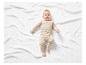 Un bébé dans un ensemble beige allongé sur une couverture blanche.