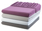 Une pile de draps de lit de différentes couleurs, dont du violet, du gris et du blanc.
