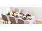 Table dressée avec bols de soupe et plats de légumes, chaises rembourrées beiges.