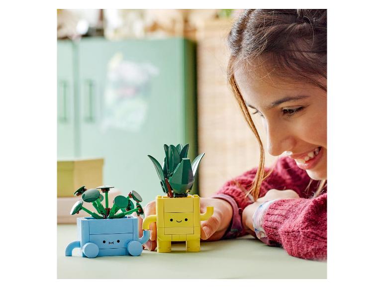 Une fille souriante joue avec deux plantes jouets, une bleue et une jaune.