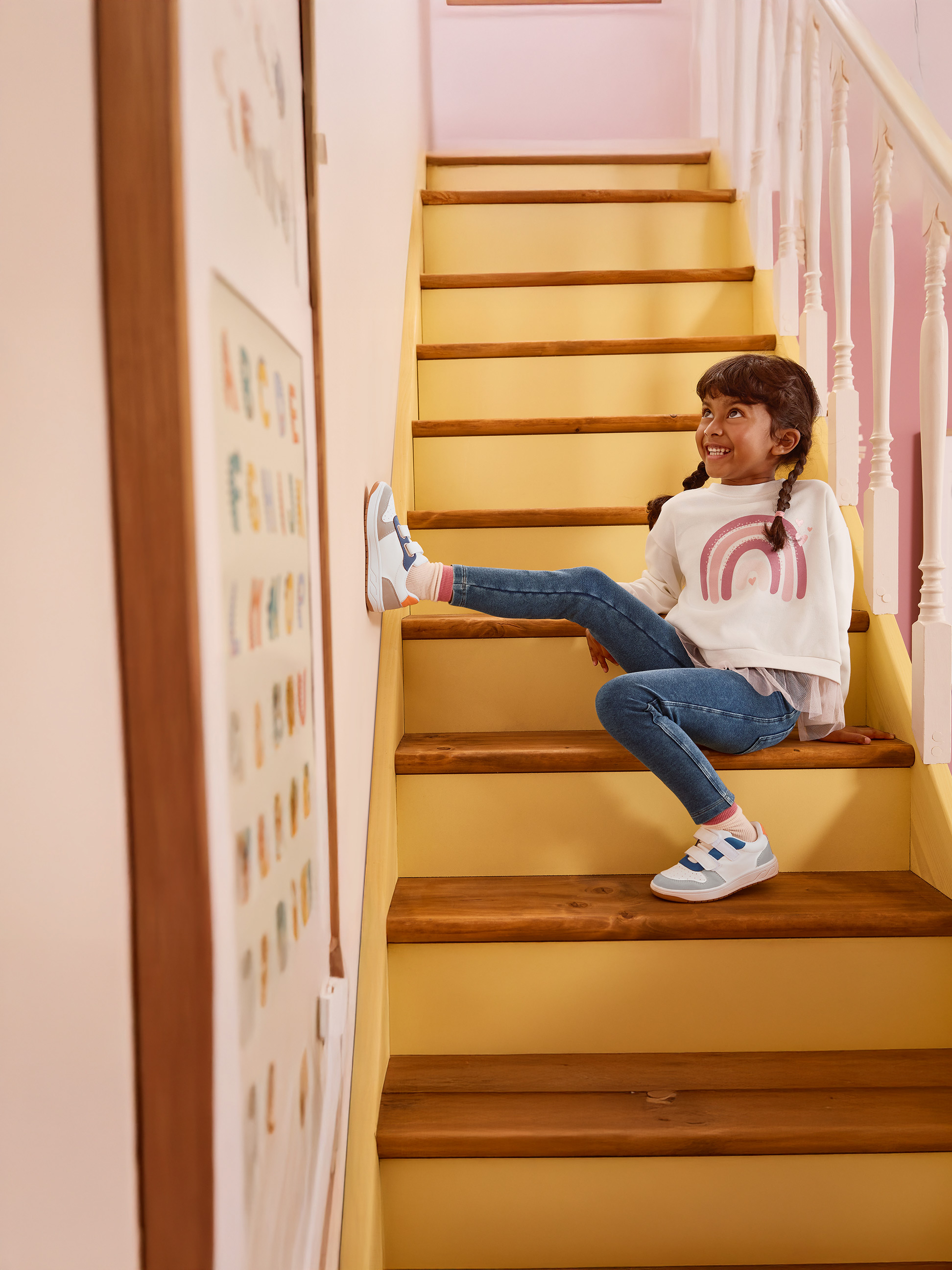 Fille en sweat-shirt arc-en-ciel blanc et jean bleu assise sur des escaliers en bois