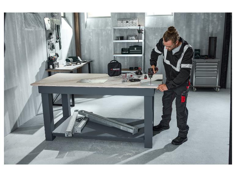 Homme en pantalon de travail PARKSIDE PERFORMANCE® perçant dans un atelier.