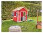 Maisonnette de jeu en bois rouge avec bac à sable et jouets d'extérieur dans un jardin vert.