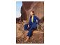 Femme en costume bleu et haut jaune, assise sur des rochers dans un paysage désertique.