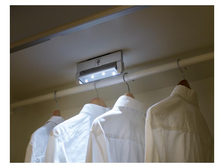 Chemises blanches accrochées à des cintres dans un placard éclairé par un luminaire de plafond.