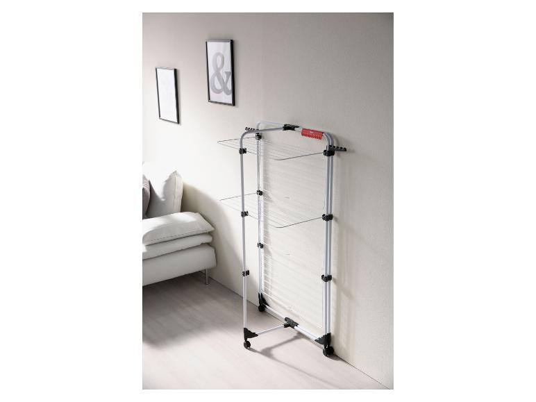 Séchoir à linge blanc à trois niveaux, à côté d'un canapé gris clair et d'art encadré.