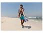 Homme en short de bain et serviette marchant sur la plage.