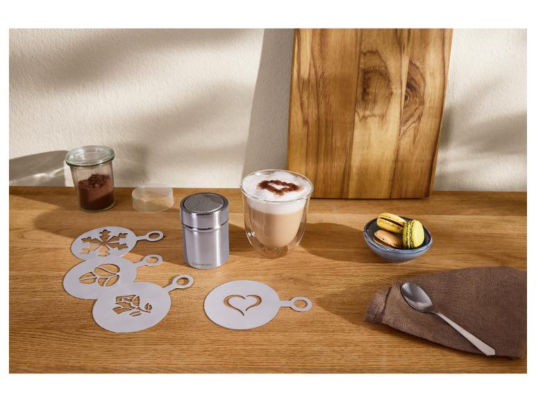 Pochoirs à café et saupoudreur de cacao avec un latte et des macarons sur une table en bois.