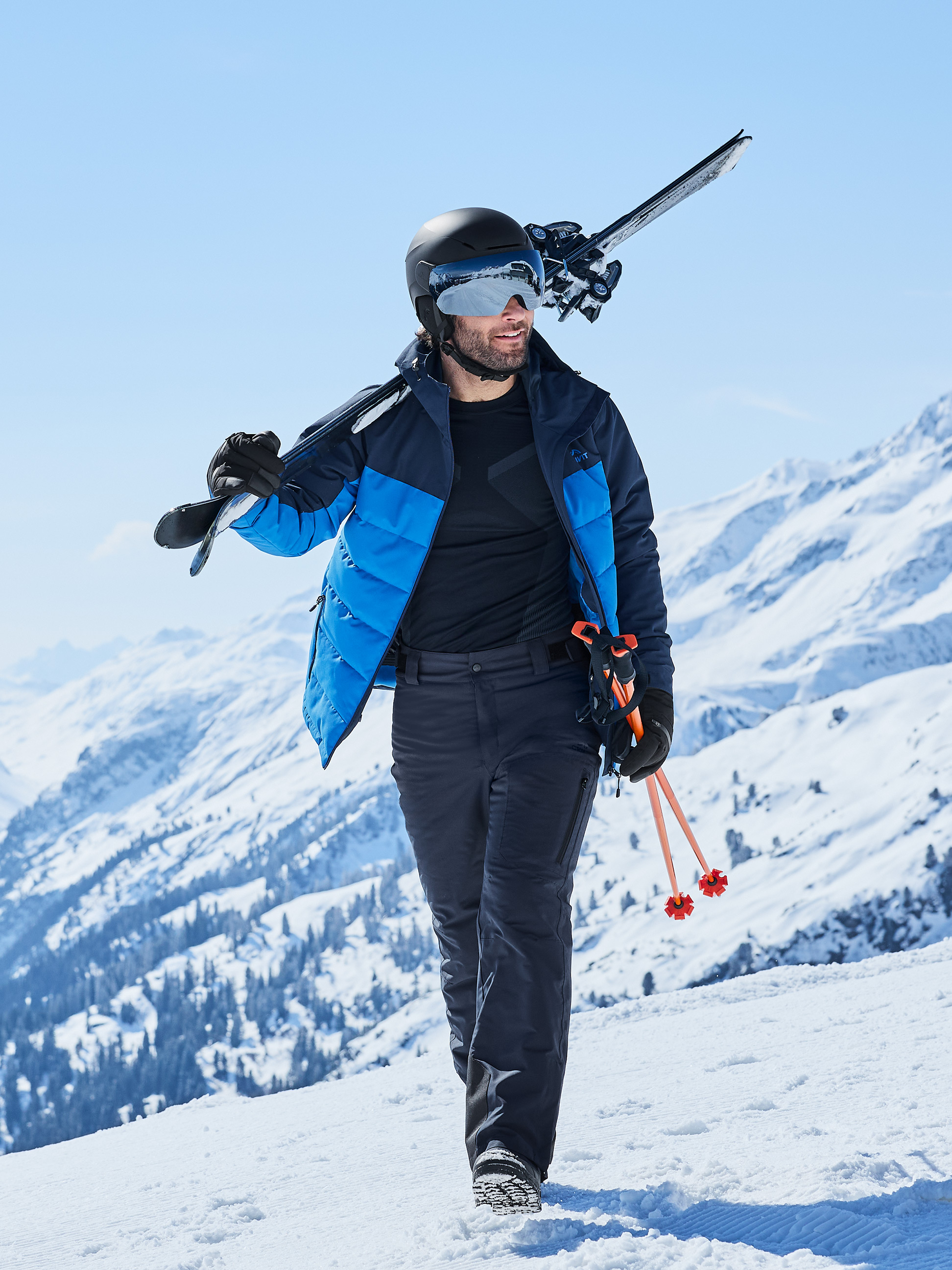 Homme en veste de ski, pantalon et casque avec skis et bâtons dans la neige.