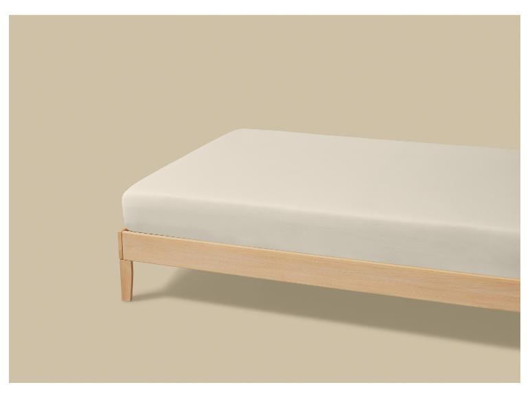 Un matelas de couleur claire sur un cadre de lit en bois sur fond beige.