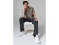 Un homme portant une chemise à imprimé, un pantalon noir et des baskets Vans blanches.