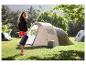 Femme tenant un sac de couchage, debout à côté d'une tente de camping et d'une glacière.