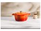 Cocotte orange dégradée sur un comptoir en marbre blanc avec deux bocaux en arrière-plan.