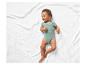 Bébé sur une couverture blanche portant un body vert.