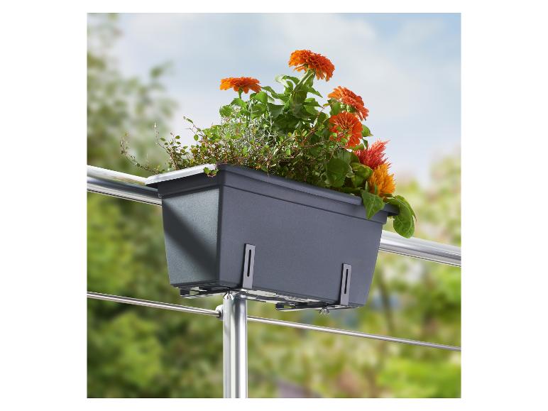 Jardinière de balcon grise avec fleurs oranges et plantes vertes, fixée à une balustrade.