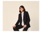 Femme en blazer noir et chemise blanche assise sur une chaise.