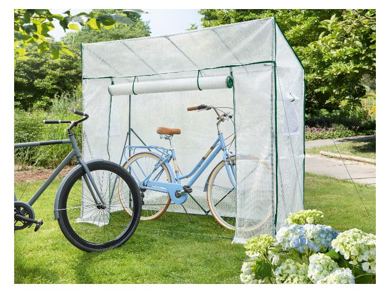 Deux vélos, un bleu clair et un gris, rangés dans un abri à vélos transparent sur une pelouse.