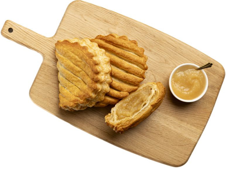 Chaussons aux pommes dorés et bol de compote de pommes sur une planche en bois.