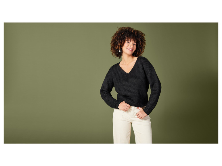 Une femme porte un pull noir et un pantalon blanc.