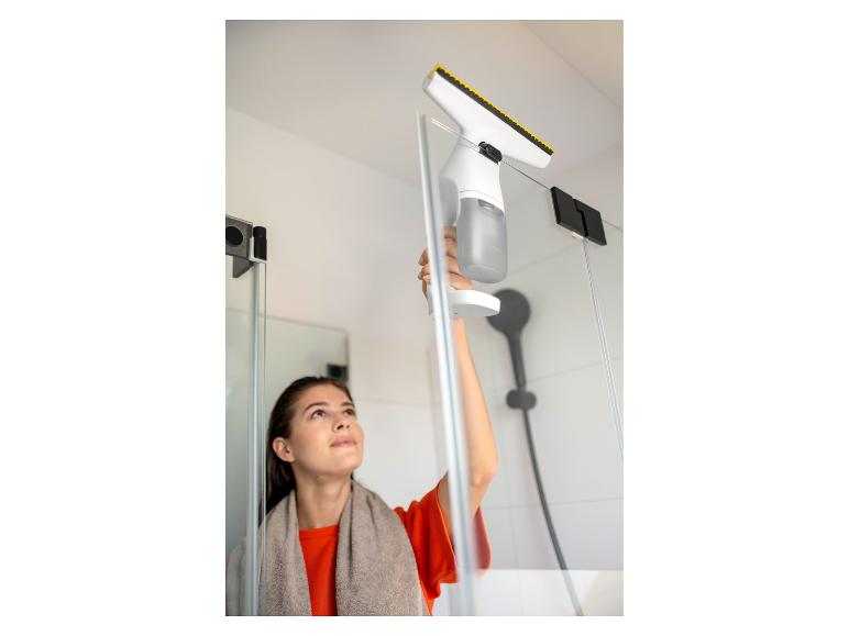 Femme nettoyant une paroi de douche avec un nettoyeur de vitres électrique.