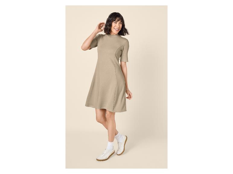 Femme souriante en robe beige à manches courtes et baskets blanches.