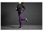 Une femme courant avec un pull noir et un legging violet.