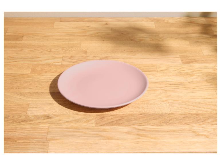 Assiette rose sur une table en bois clair avec lumière du soleil et ombres.