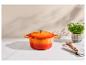 Marmite en fonte orange avec couvercle, manique, cuillère en bois et persil en pot sur une surface en marbre.