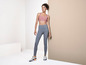 Une femme portant des vêtements de sport, dont un soutien-gorge de sport rose et un legging gris.