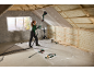 Femme ponçant un plafond avec une ponceuse télescopique dans un grenier en rénovation.