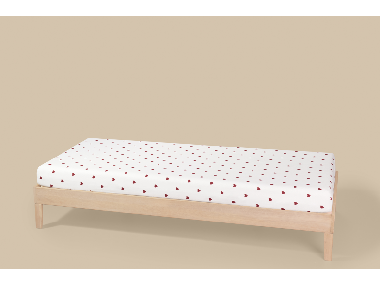 Drap-housse blanc à cœurs rouges sur un lit en bois.