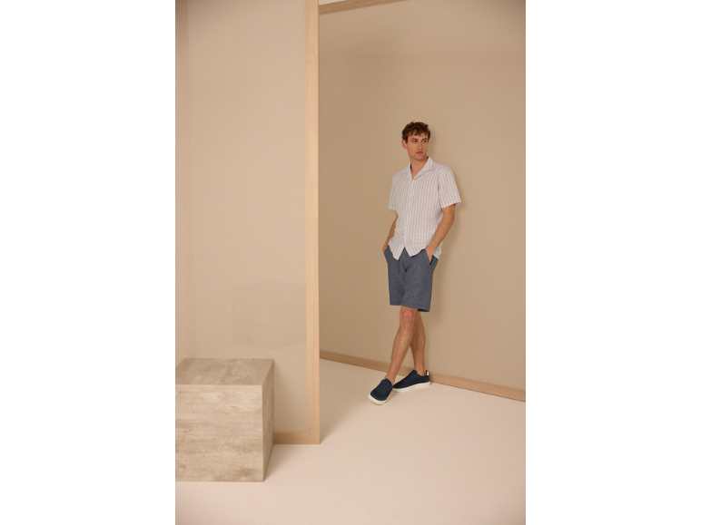 Homme portant une chemise rayée, un short bleu et des baskets.