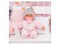Poupée bébé en pyjama rose avec sucette et biberon, assise dans un berceau blanc.