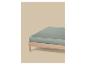 Un drap-housse vert clair sur un cadre de lit en bois sur fond beige.