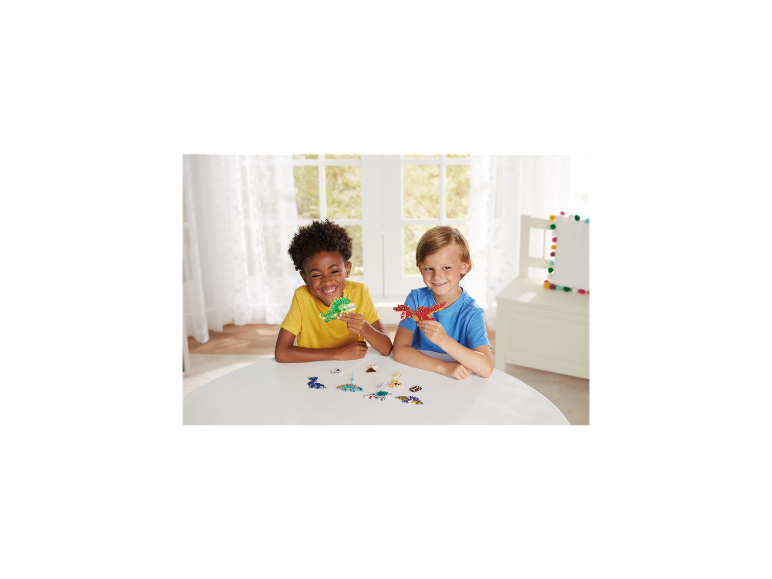 Deux garçons jouent joyeusement avec des créations d'art en perles colorées à une table blanche.